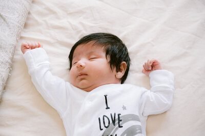 A sleeping newborn resting on a light blanket in a white outfit