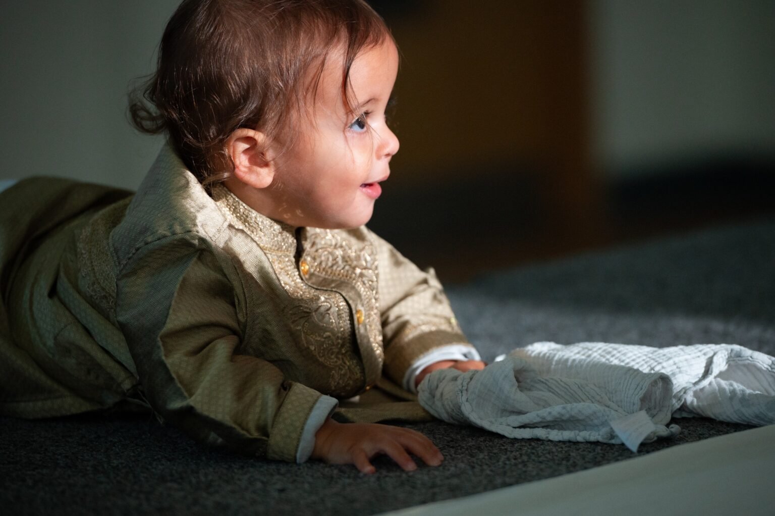 An older baby in a patterned outfit looking to one side