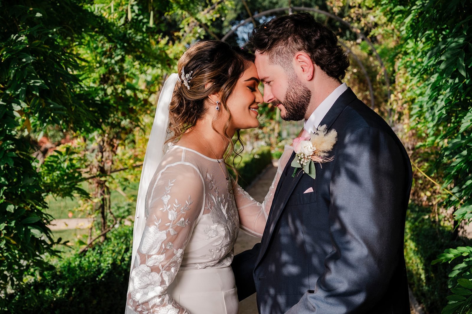 Bride and groom touching foreheads beneath leafy trees