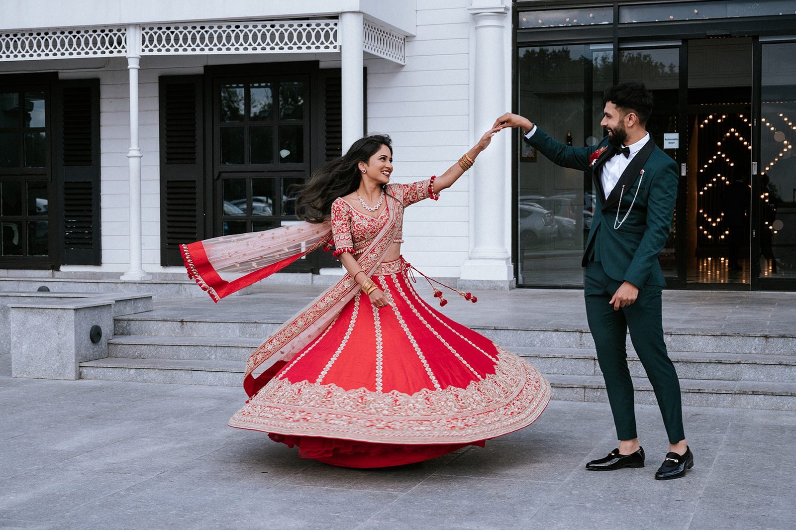 Couple dancing outside a venue, with a red embroidered lehenga and dark green suit