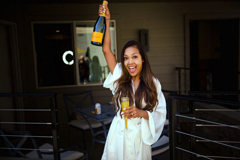 Bride raising a champagne bottle during wedding morning preparations