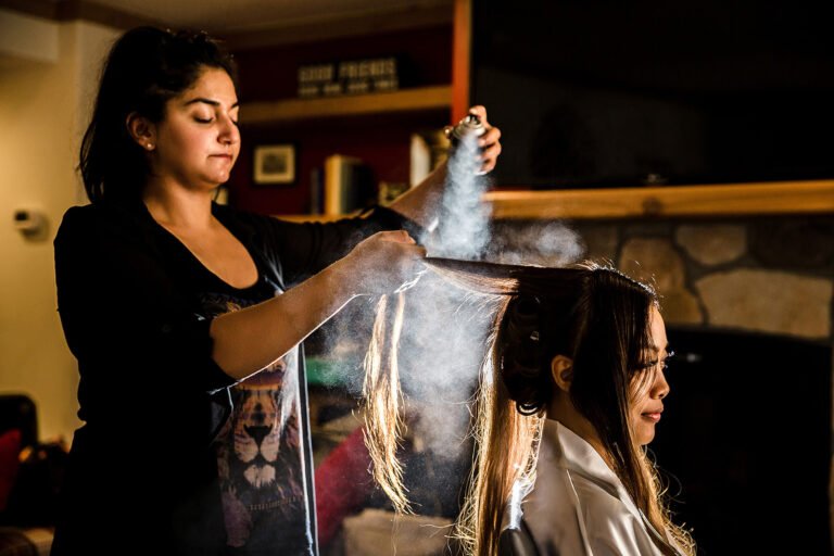 Wedding hairstylist preparing the bride in dramatic window light
