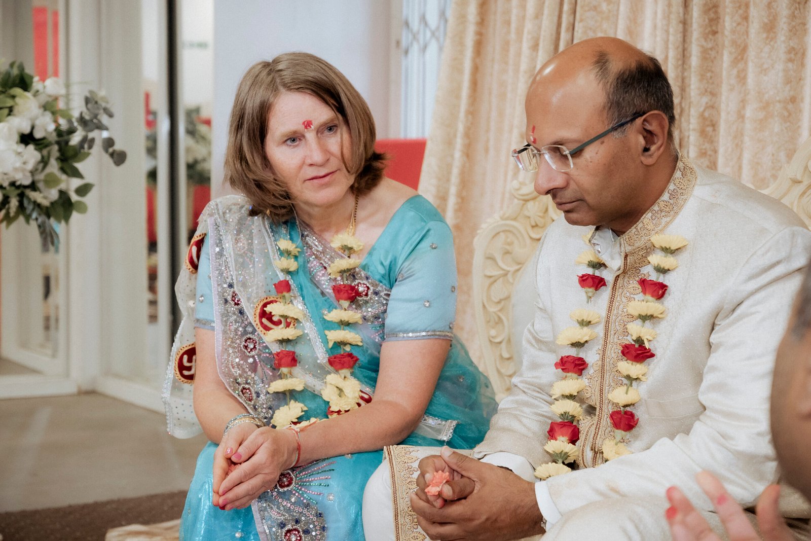 Relative applying a chandlo tilak blessing to the forehead while family members support the couple during a Gujarati Mandvo ceremony in Birmingham