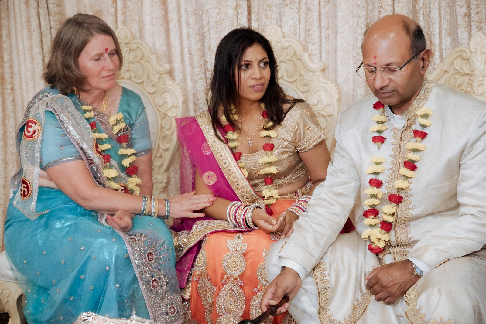 Bride-to-be in an orange and gold lehenga smiling up at her family as blessings are shared during a Gujarati Mandvo ceremony in Birmingham