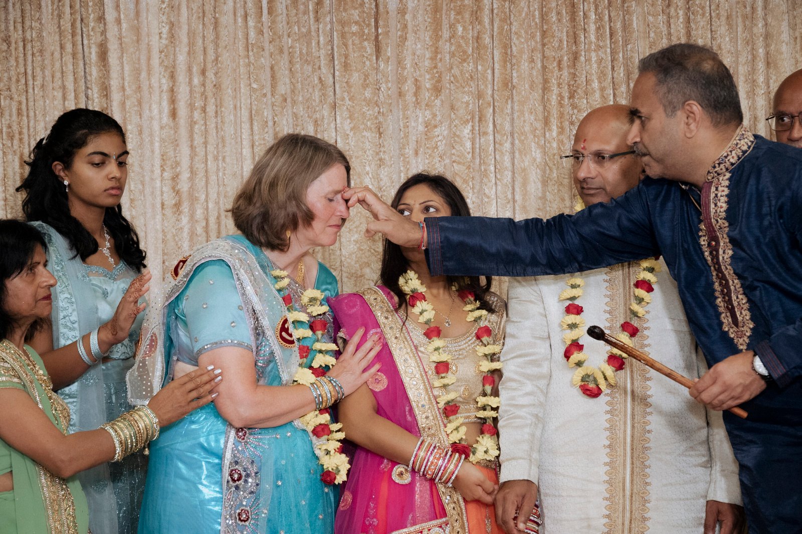 Three generations of a family in traditional Indian wedding outfits photographed together during a Gujarati Mandvo ceremony in the UK