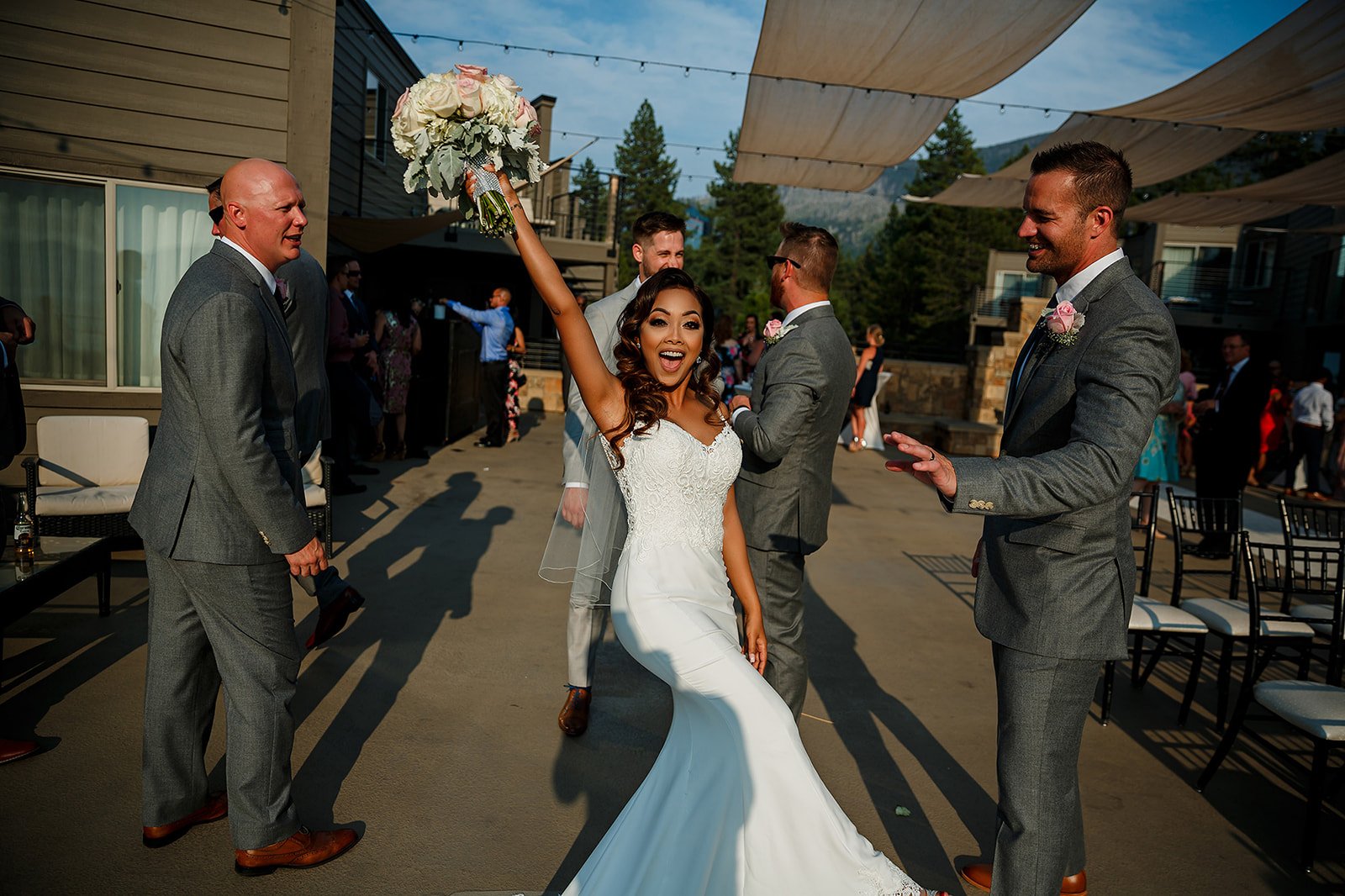 Bride raising her rose bouquet beside the groom and wedding guests