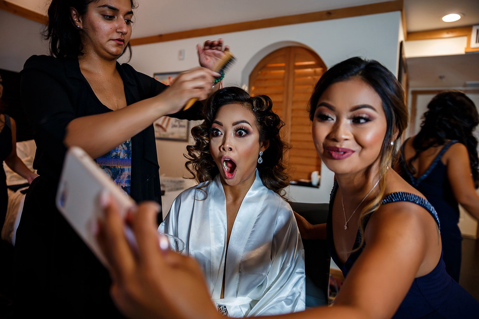 Bride laughing with a bridesmaid while a stylist finishes her hair