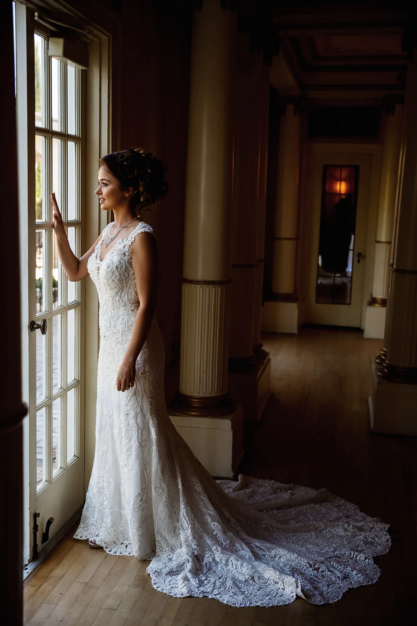 Bride standing in window light with the full train of her wedding dress