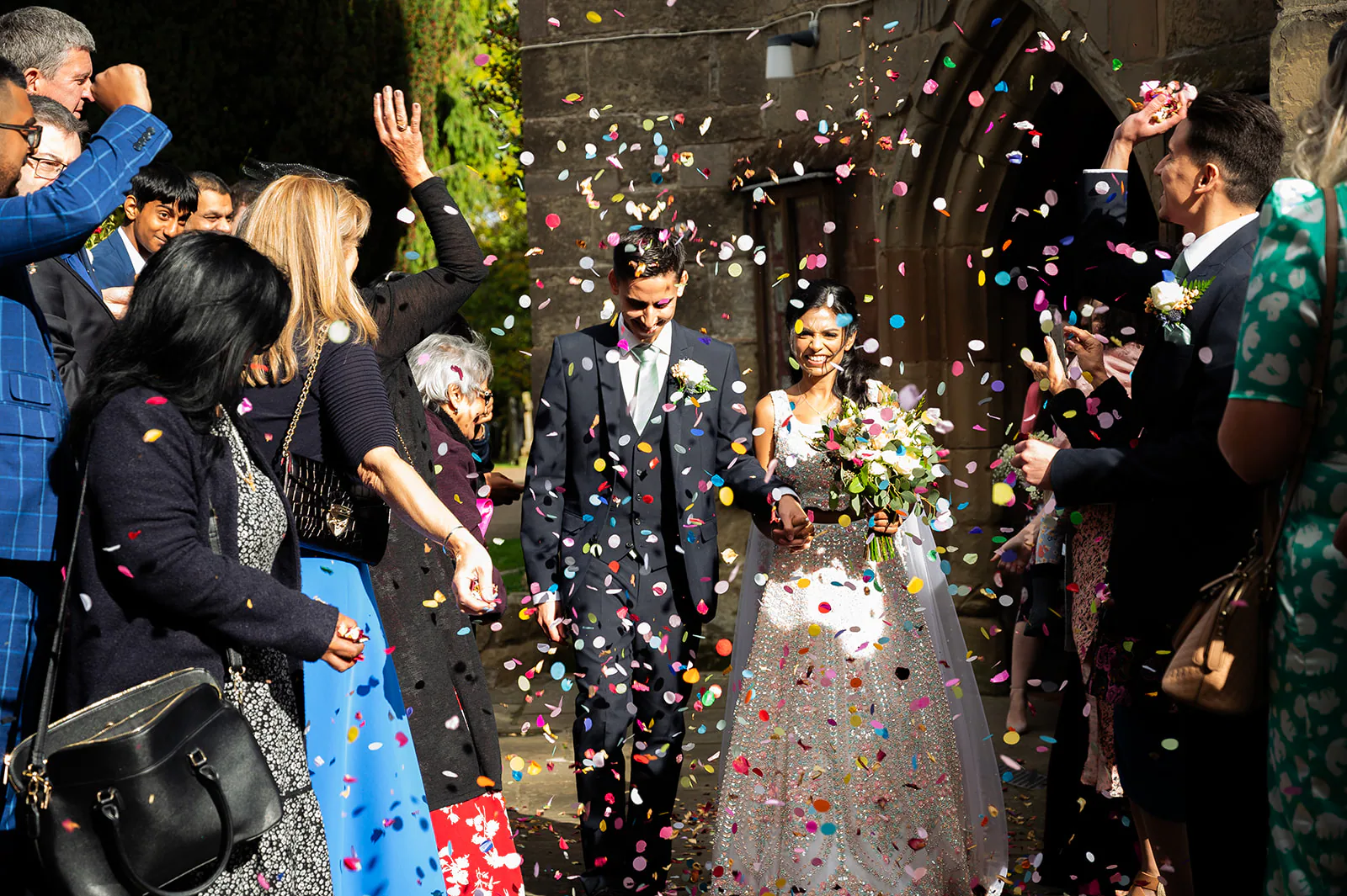 Bride and groom leaving a church through colourful wedding confetti