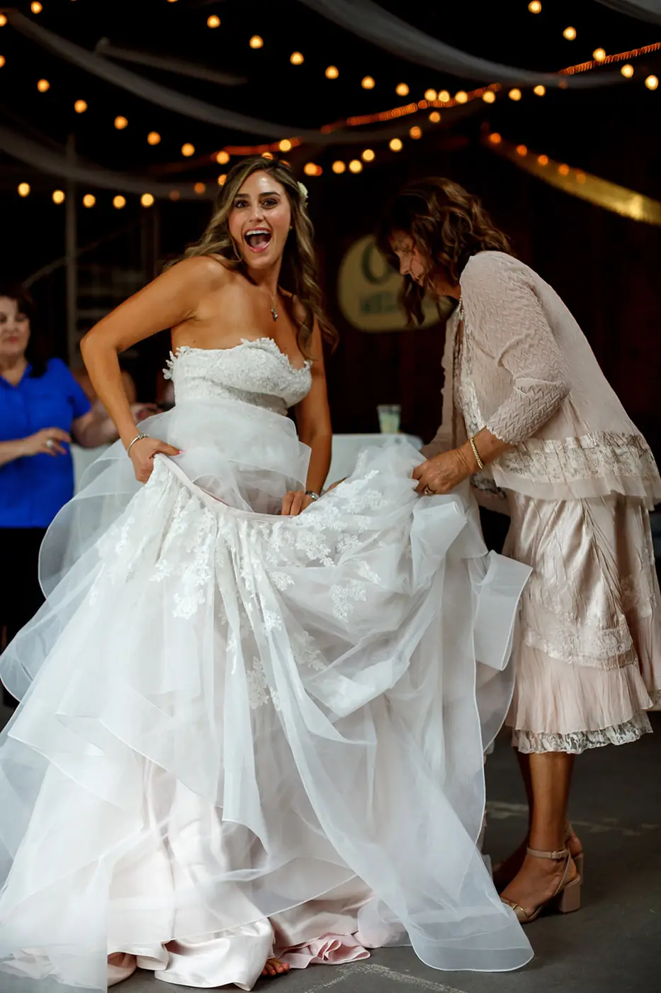 Bride lifting her skirt while a guest helps arrange the wedding dress