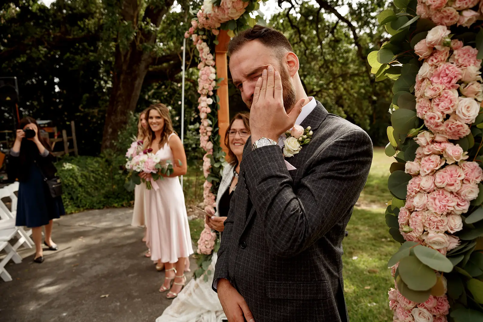 Groom wiping away a tear beneath an outdoor ceremony arch