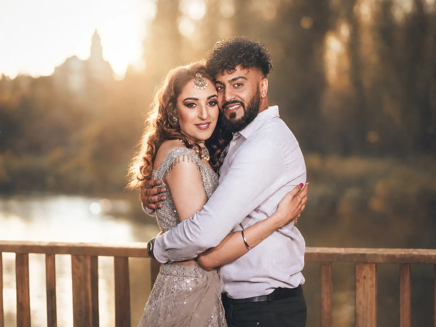 Engaged couple embracing on a wooden bridge beside a lake at sunset