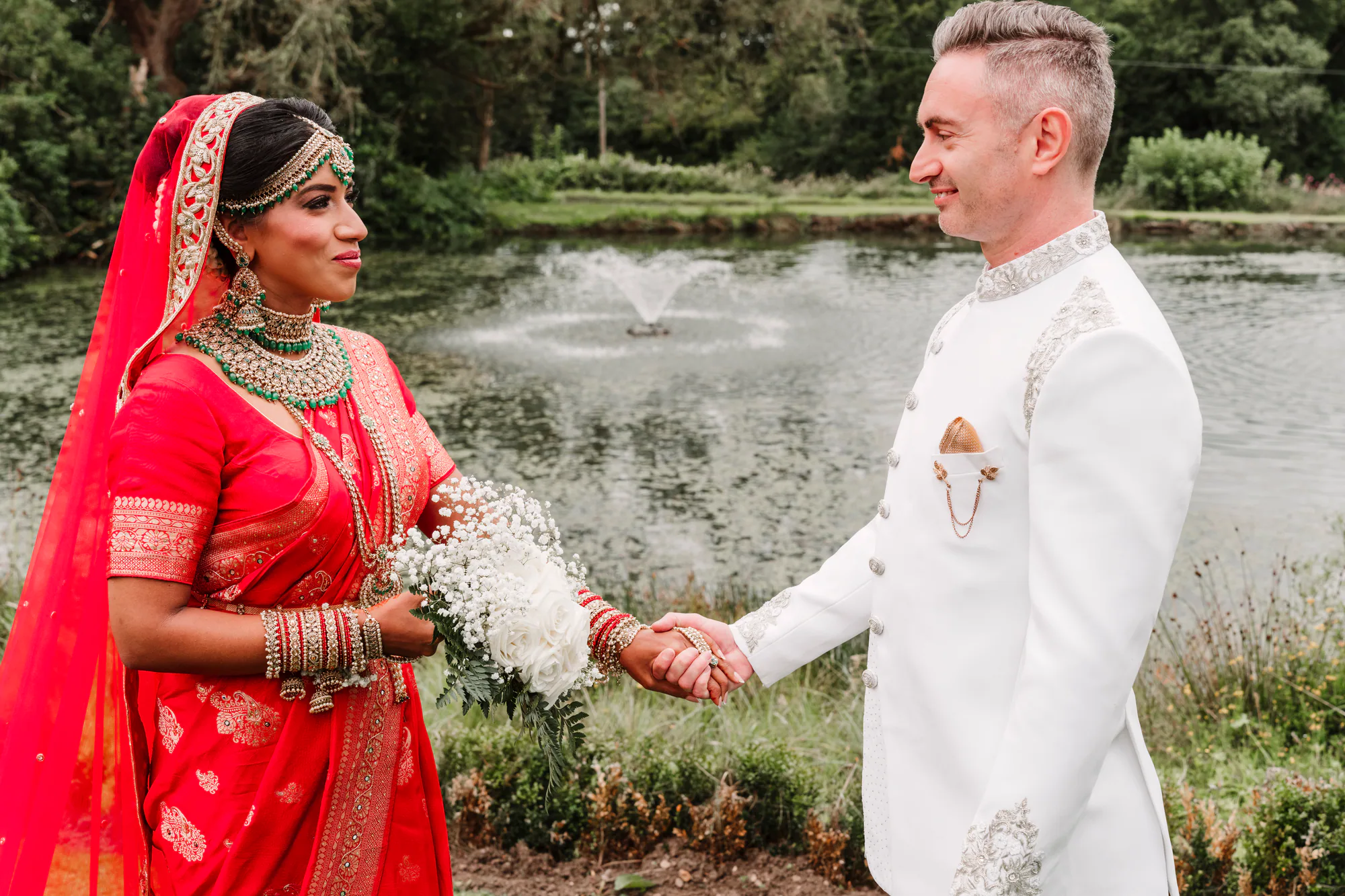 Indian fusion wedding couple holding hands beside a lake