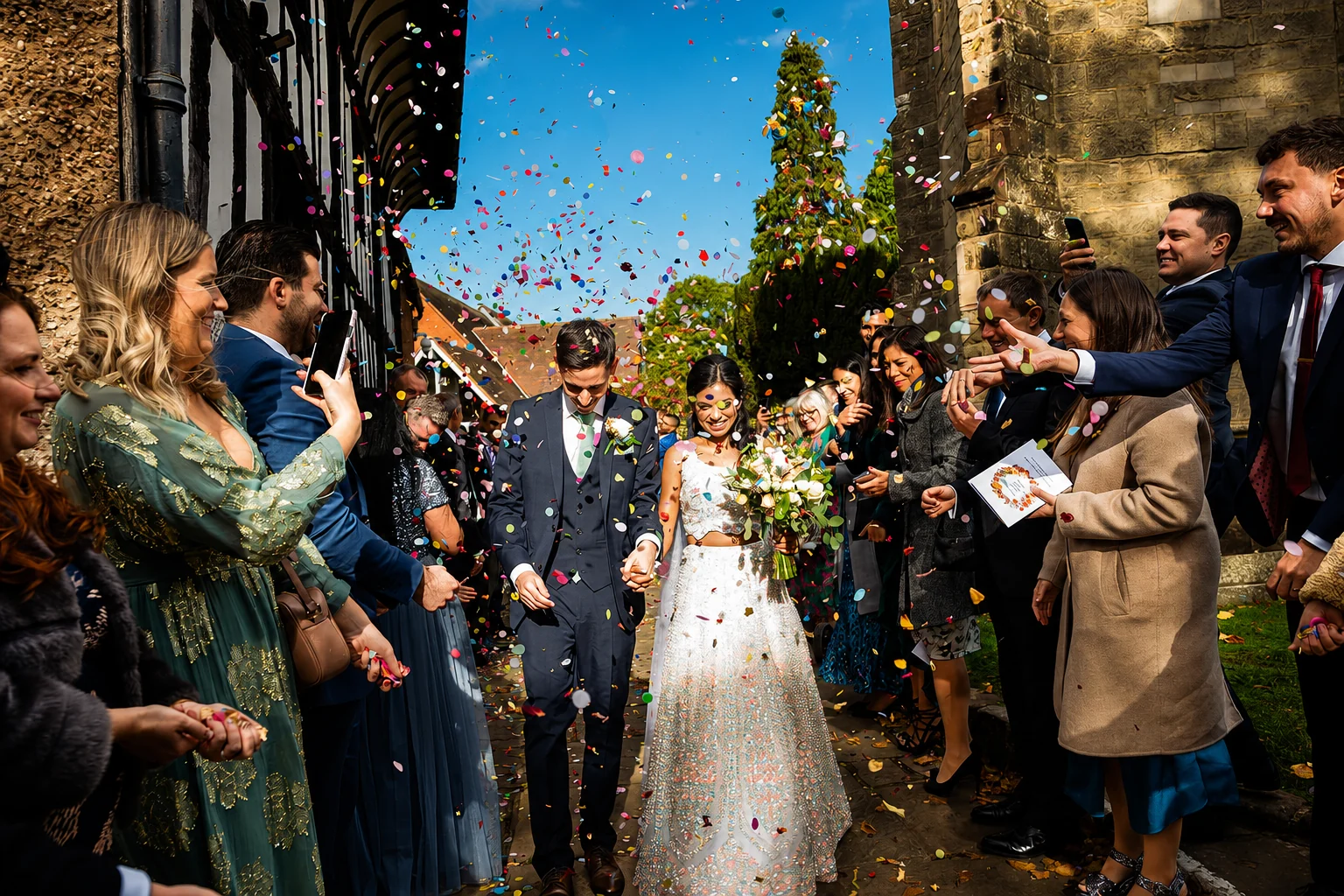 Newlyweds walking through colourful confetti outside a church