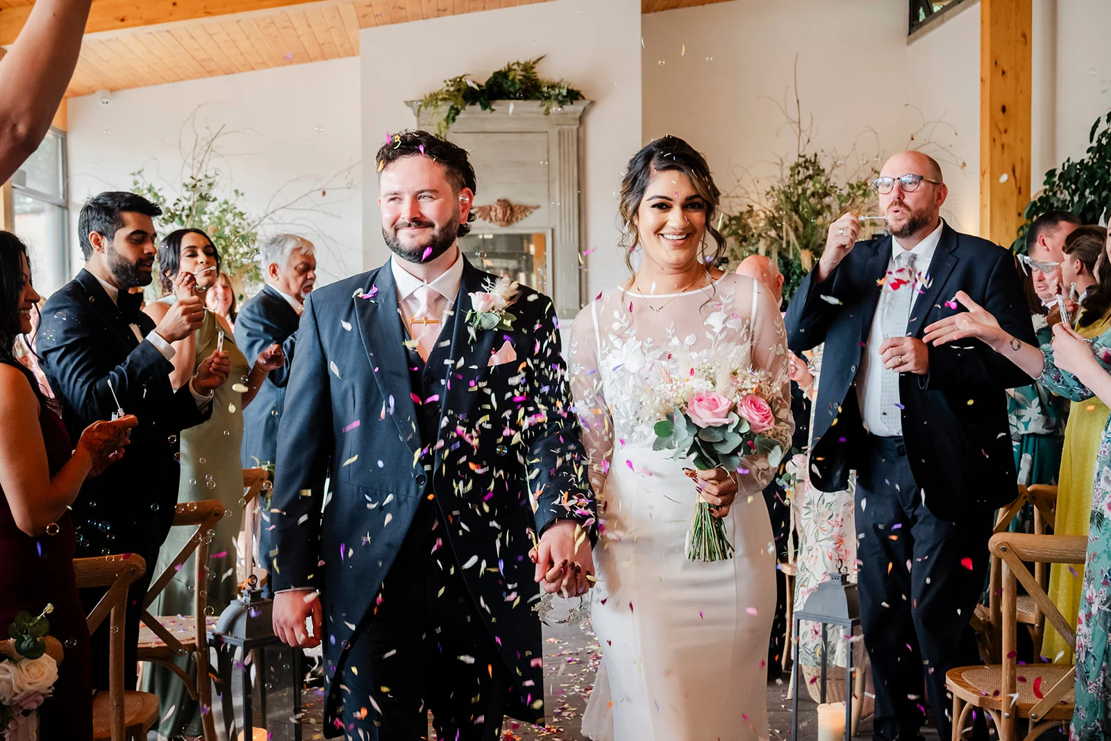 Newlyweds smiling as guests shower them with confetti after their ceremony