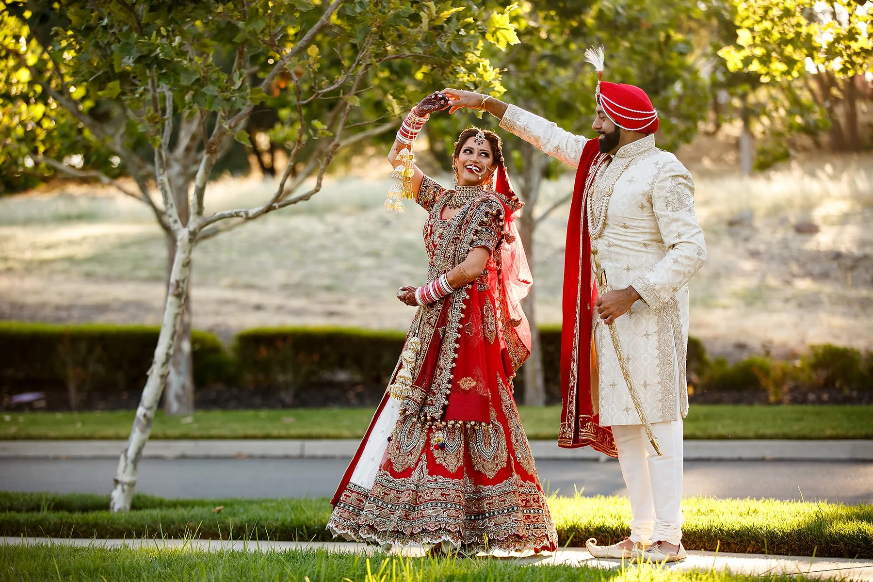 Bride in a red lehenga twirling with her groom in a sunlit garden in Dar es Salaam