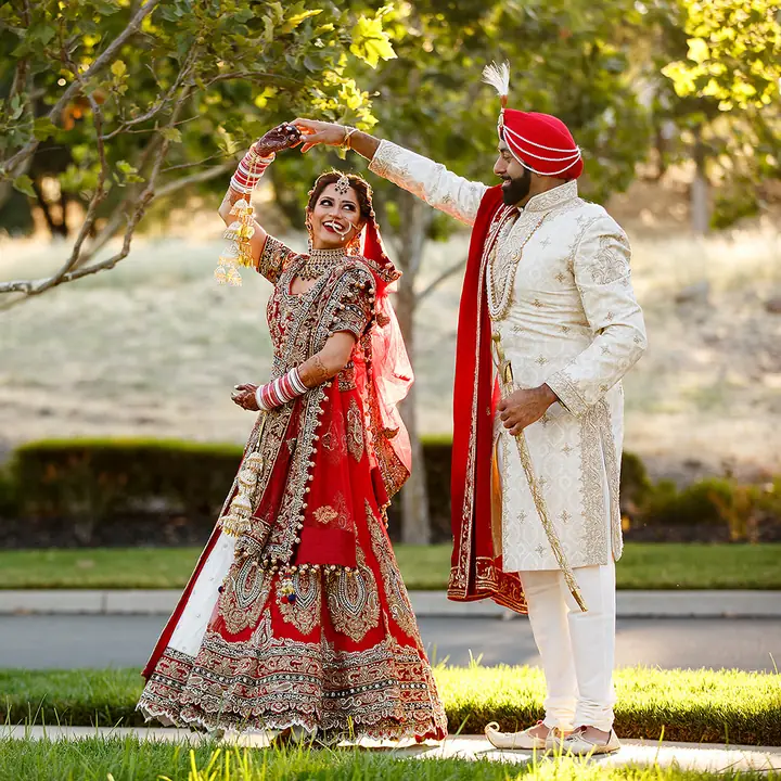 Groom in an ivory outfit and red turban twirling his bride outdoors
