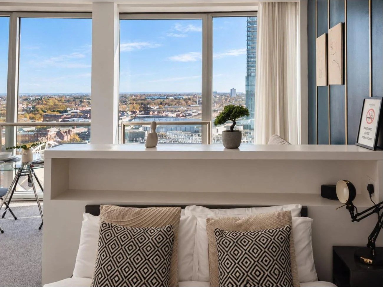 Headboard shelf styled with a bonsai and ornaments against Birmingham skyline windows, Airbnb listing photo