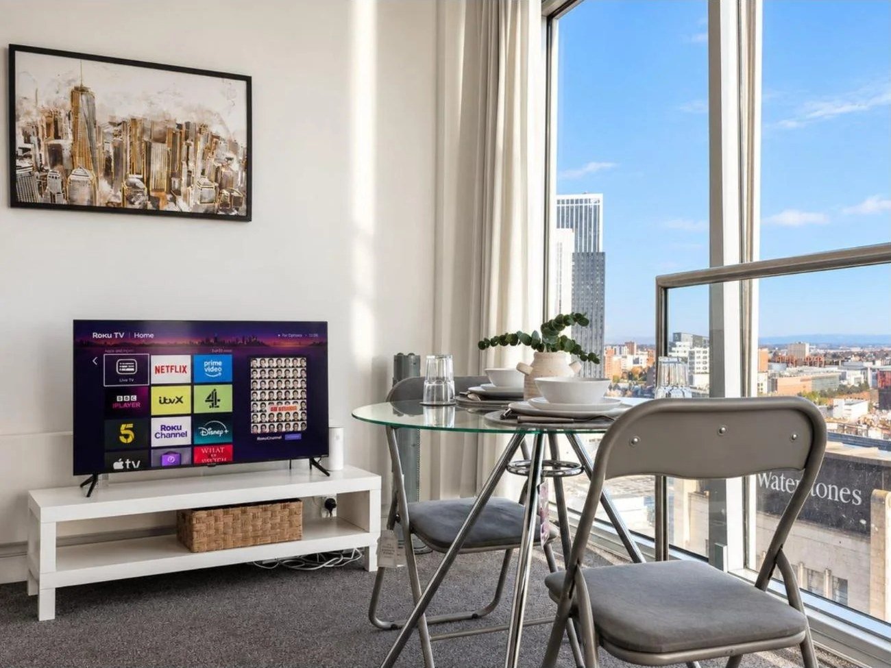 Living and dining area of a Birmingham city centre Airbnb with smart TV and glass dining table by the window