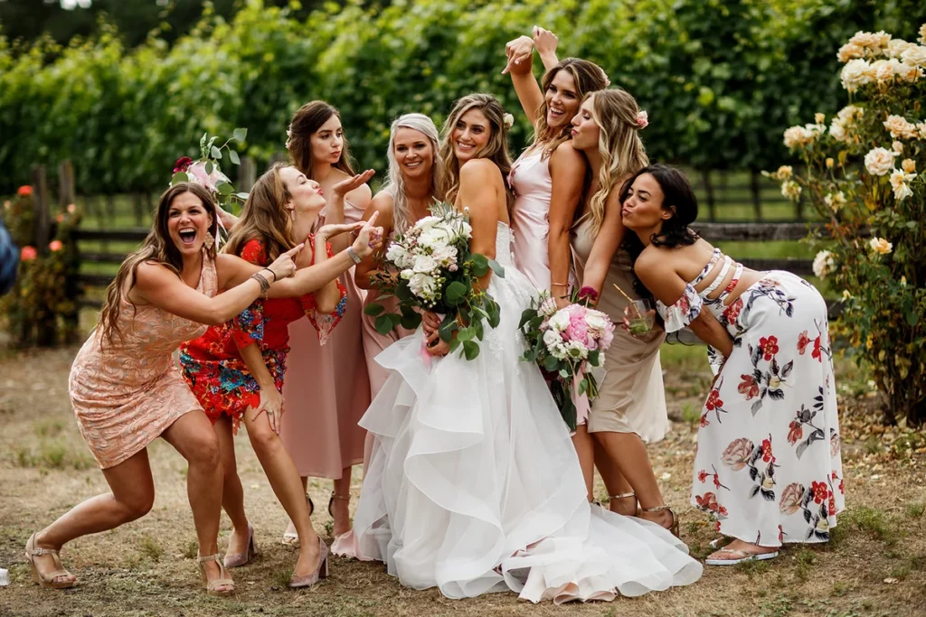 Bride and her friends laugh and pose together with bouquets in a garden
