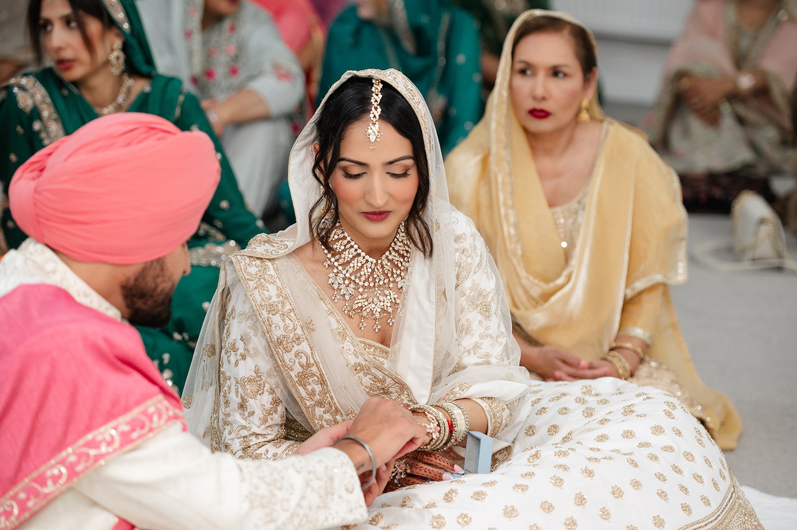 Bride looking down during the Anand Karaj with family seated behind her