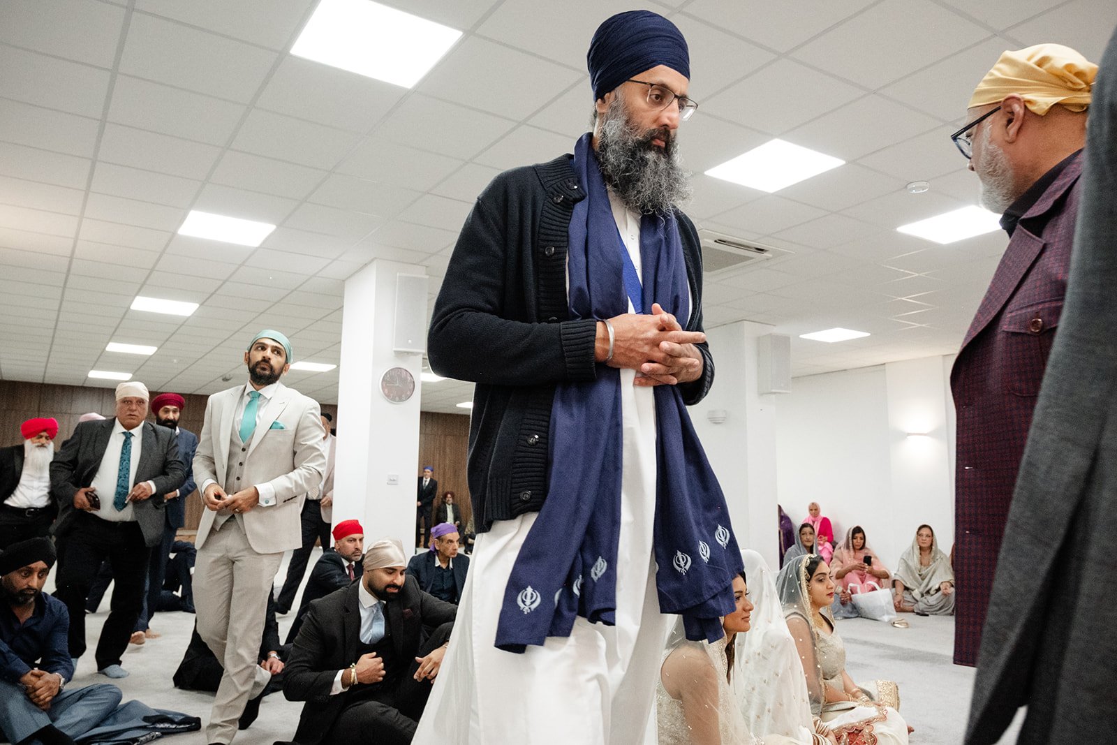 Wedding guest in a navy turban receiving a small serving during the Sikh celebration