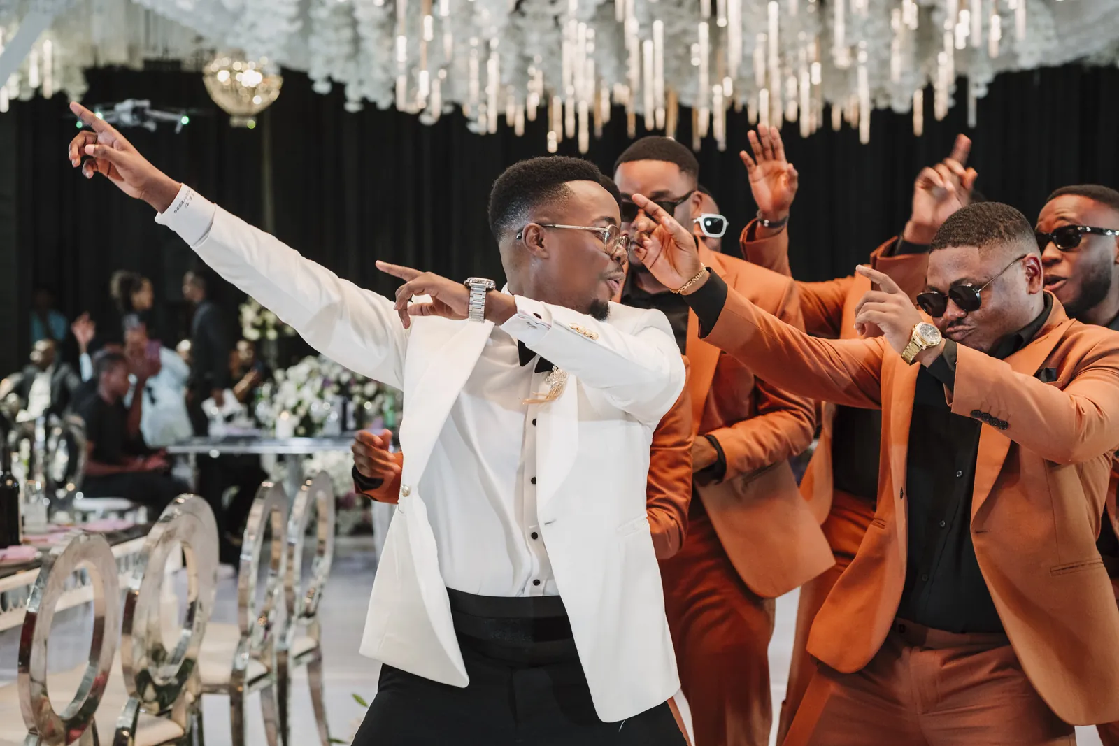 Groom in a white tuxedo jacket dancing with his groomsmen at a wedding reception